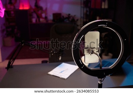 Organized workspace setup including ring light, microphone, smartphone, notes on desk suitable for podcasting or streaming with creative ambiance enhancing atmosphere