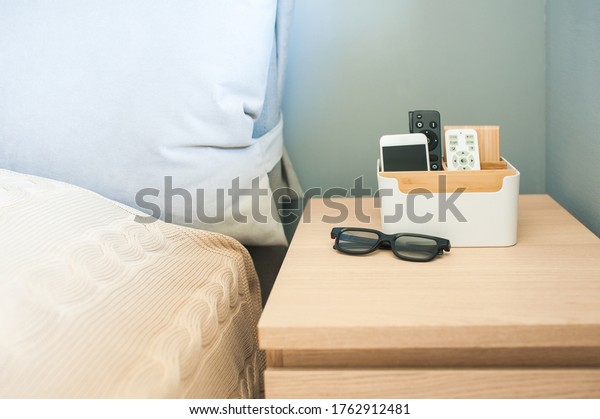 Organizer box for storing personal belongings,\
stands on the bedside table near the bed. Inside the phone, a\
remote control for light, near\
glasses.