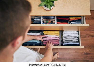 Organizing and cleaning home. Man preparing orderly folded t-shirts in drawer. 
