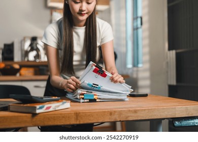 Organizing documents on wooden desk, woman carefully arranges colorful files and papers. workspace is bright and modern, reflecting productive atmosphere. - Powered by Shutterstock