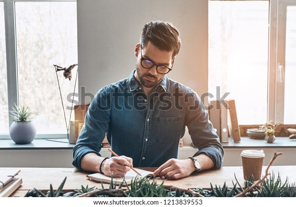 Organizing\
every minute. Thoughtful young man writing something down in\
personal organizer while sitting in the\
office