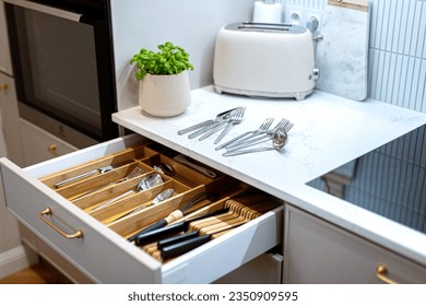 Organizing silver cutlery and kitchenware in kitchen drawer. Storage organization system in kitchen cabinets. Tidying up cutlery tray
