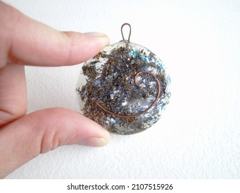 Orgone Pendant With Auric Copper Spiral And The Hindu Symbol Of The 5th Chakra Vishuddha Held By A Female Caucasian Hand. Harmonizer Of Energy Fields. Ion And Proton Stabilizer.