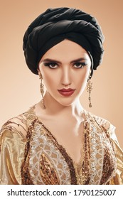 Oriental Beauty Woman. Portrait Of A Beautiful Arabian Woman In Golsen Top With Traditional Oriental Make-up And Black Turban. Make-up And Cosmetics. 