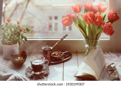 Oriental Coffee Cooked In Traditional Turkish Copper Coffee Pot With Flowers On Window Sill. Wooden Windowsill With Bunch Of Tulips, Old Book. Cold Rainy Day In Spring. Cozy Scene, Hygge Concept.