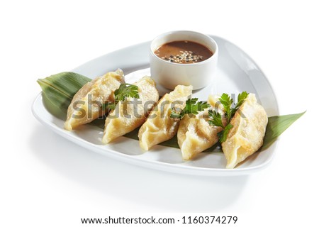 Oriental Fried Dim Sum with Minced Meat also known as Gyoza, Dim Sum, Jiaozi or Momo on a Banana Leaf with Spicy Sauce Close Up. Hot Crunchy Deep-Fried Beef and Mutton Dimsum Isolated on White