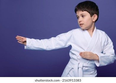 Oriental martial arts. Waist length portrait of an aikido wrestler European 10 years old boy in white kimono improves his fighting skills, isolated on purple background with copy ad space