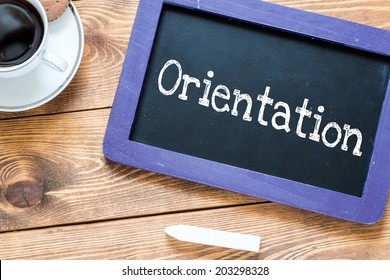 Orientation handwritten with white chalk on a blackboard, cup of coffee and biscuit on a wooden background  - Shutterstock ID 203298328