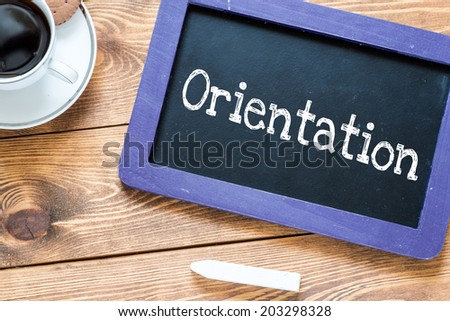Orientation handwritten with white chalk on a blackboard, cup of coffee and biscuit on a wooden background 