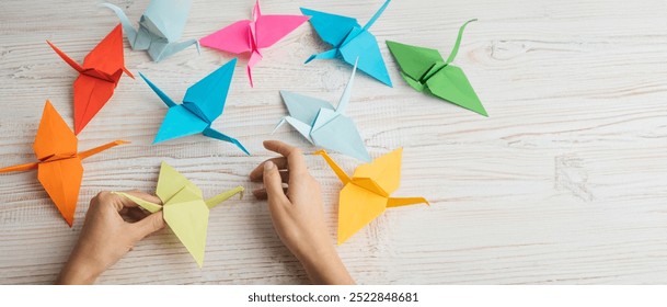 Origami art. hands holding colorful origami cranes from paper with white wooden table at the background. Paper sculpture through folding and relaxing techniques - Powered by Shutterstock