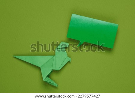 Origami dinosaur with empty speech bubble on green background