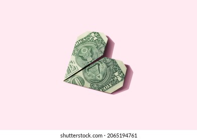 Origami Dollar Heart Isolated On Pastel Pink Background. Minimal Finance Money Business Aesthetic Concept Poster Or Banner.