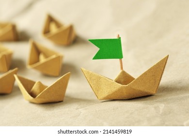 Origami recycled paper boat with green flag leading a group of small boats - Concept of leadership, teamwork and ecology