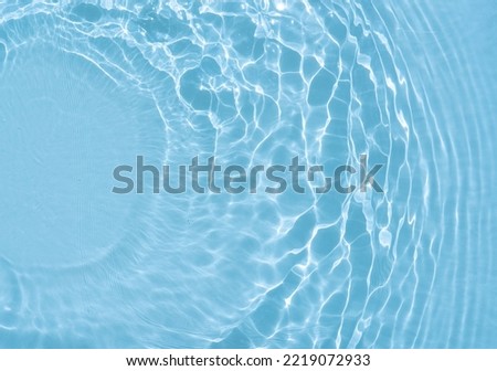 Original beautiful background image in blue tint for creative work or design in form of water surface with diverging circular waves, play of light and shadow and space for text. Water texture.