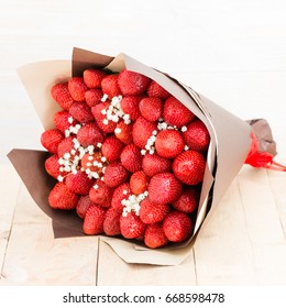 the original bouquet of strawberries with little white flowers on wooden table, light background