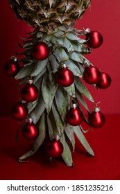 Original Christmas tree concept. Red shiny glass baubles hangs on the leaves of ripe pineapple standing upside down. Red festive background.