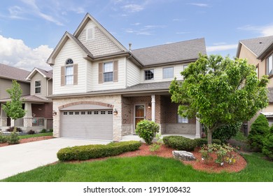 ORLAND PARK, IL, USA - MAY 20, 2019: A New Suburban House With Half Light Brown Siding And Have Brick And Stone, Brown Window Shutters, And A Front Porch.