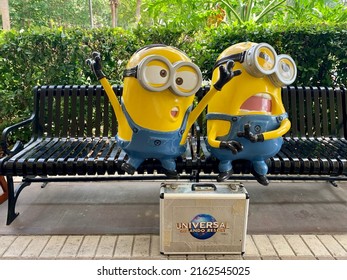 Orlando, FL, USA, 3.15.22 - The close up image of two minions sitting on a metal park bench with a briefcase that has Universal Orlando Resort printed on it.