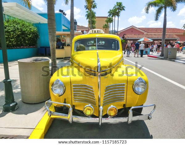 Orlando, Florida,\
USA - May 10, 2018: The people going near yellow retro car taxi at\
Universal Studios Orlando. Universal Studios Orlando is a theme\
park resort in Orlando,\
Florida.