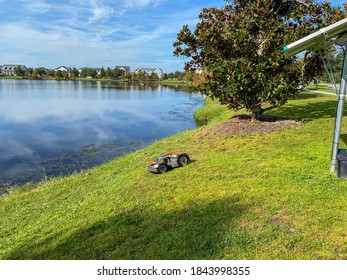 Orlando, FL./USA - 10/16/20:  A Husqvarna Autonomous Lawn Mower Mowing Near A Lake In The Laureate Park Neighborhood In Orlando, Florida