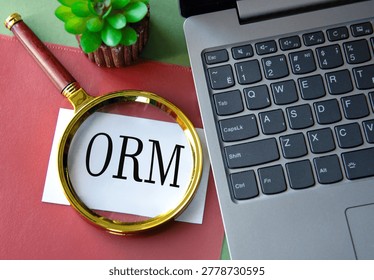 ORM ( Object-Relational Mapping) - acronym on a white sheet under a magnifying glass next to a laptop