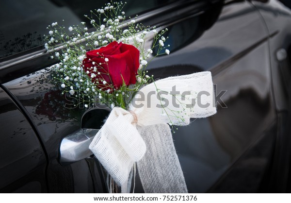 Ornament of red rose\
with white bow nicely decorates silver handle of black wedding car.\
Ceremony detail\
concept