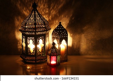 Ornamental Arabic lanterns. Burning candles on table glowing at night. Festive greeting card, invitation for Muslim holy month Ramadan Kareem. Iftar dinner background with golden glow.