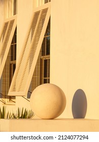 Ornamental Concrete Sphere, About The Size Of A Beach Ball, And Its Sunset Shadow By Tall Hurricane Shutters On A Concrete House In An Upscale Beach Town Along The Gulf Coast In The Florida Panhandle