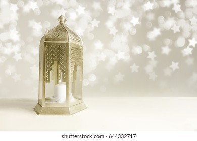 Ornamental golden Arabic lantern on the table with glittering star shaped bokeh lights. Greeting card for Muslim community holy month Ramadan Kareem. Festive blurred background with empty space.