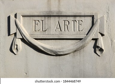Ornamental sign in relief carved on white stone with the word "art" written in Spanish: "El arte" framed in a rectangle with a ribbon