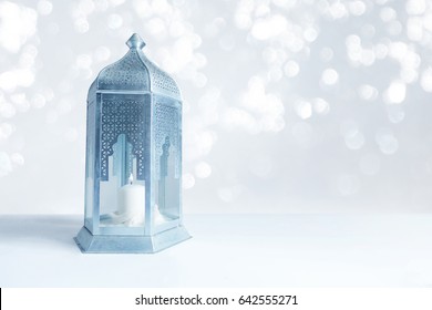 Ornamental silver and blue Arabic lantern on the table with glittering bokeh lights. Greeting card for Muslim community holy month Ramadan Kareem. Festive blurred background with a lot of empty space.