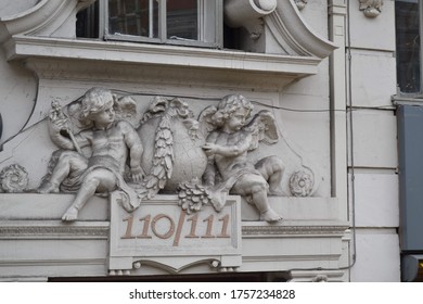 Ornate carving of cherubs above a building number on a white stone European building.