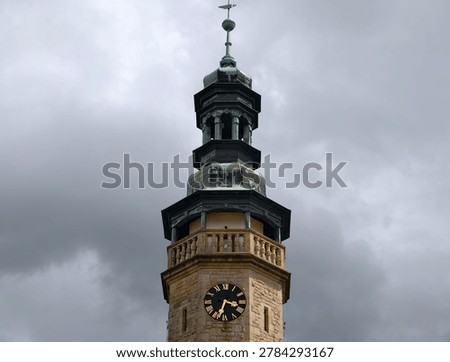 Ornate clock tower under stormy sky, historic municipal landmark with prominent clock dial, verdigris copper