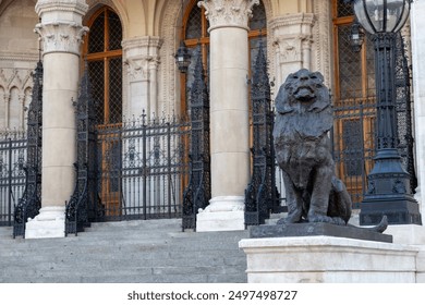 Ornate entrance of the Hungarian Parliament Building in Budapest, featuring grand columns, intricate ironwork, and a majestic lion statue guarding the steps - Powered by Shutterstock