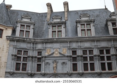 Ornate facade of a historic building in Grenoble, France, featuring intricate stone carvings, large windows, and a central statue under a cloudy sky - Powered by Shutterstock