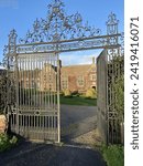 The ornate gates of Littlecote House, a stately Tudor manor in Berkshire, frame the view to the historic residence, with its impressive facade, manicured lawns inviting visitors to step back in time