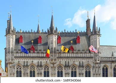 The ornate gothic city hall in Bruges with flags of Europe, Belgium, Flanders and Bruges against blue sky wiht white clouds