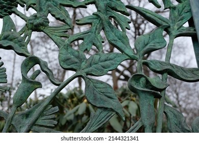 Ornate green copper gate fence with leaf and lily pattern, against tree branches and sky