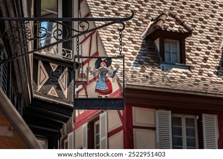 Ornate half timbered house with a wrought iron metal sign of a woman in traditional clothes in Colmar, picturesque village in Alsace France