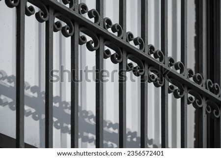 Ornate iron window grille with pattern reflected in shadows on white window surface. Abstract exterior architectural background.