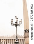 Ornate lamp post and tall obelisk in a grand plaza with colonnades