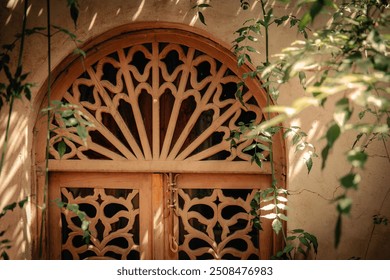 Ornate moroccan traditional wooden door with intricate lattice design, textured wall and surrounding greenery in a peaceful luxury riad courtyard with dappled sunlight, Medina, Marrakech, Morocco - Powered by Shutterstock