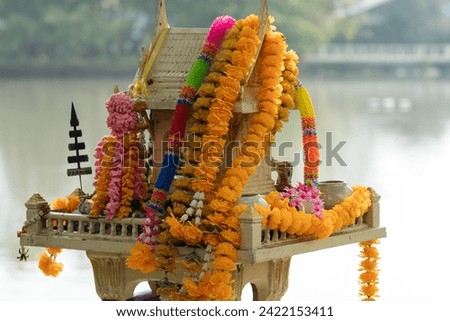 Ornate Thai spirit house adorned with colorful garlands on the river bank.