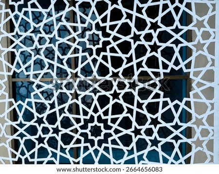 Ornate white star pattern creates a geometric lattice over window reflecting natural outdoor light. The intricate shapes create a detailed, textured effect, adding depth to the high resolution photo.
