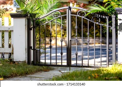 an ornate wrought iron gate between white wooden fence posts surrounded by green palm bushes