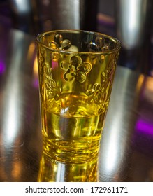 Ornate Yellow Glass With A Drink On A Metal Surface Of The Bar Counter. Reflection, Game Of Light And Shadow.