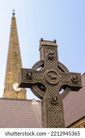 Ornately Carved Celtic Cross With Knotwork With The Clock Tower Church Steeple Behind.