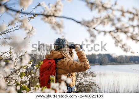 Ornithology observations. Woman with binoculars watching birds at lake during spring hiking in nature