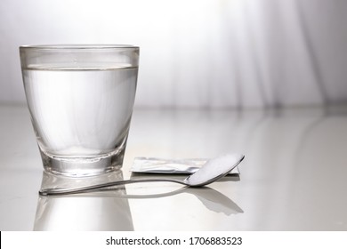 ORS Or Oral Rehydration Salt With Glass Of Water, Sachet And Spoon On Table Against Window Light