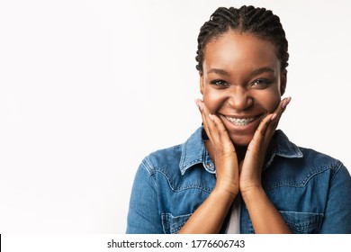 Orthodontics Concept. Joyful Black Girl With Brackets Cupping Face In Hands Smiling To Camera On White Background. Studio Shot